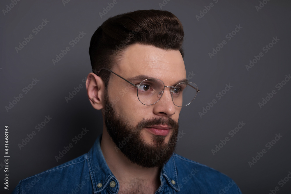 Confident smart modern bearded man in casual denim clothes and eyewear is posing over gray background in the studio Confident smart modern bearded man in casual denim clothes and eyewear is posing over gray background in the studio