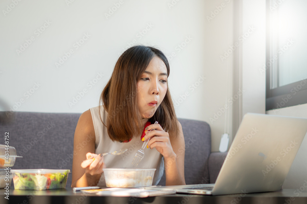Portrait of young Asian woman freelancer working with laptop at her home and eating Asian food with takeaway. Work at home during self-isolation quarantine and New normal concept.