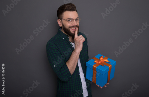 Excited handsome bearded man in casual wear in good mood with big gift box in his hands shows surprise gesture over gray background