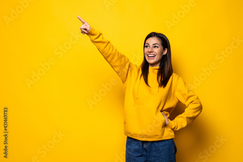 Young woman pointing finger to the side over isolated yellow background