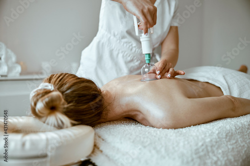 professional female specialist is doing cupping therapy on the back of beautiful caucasian lady photo