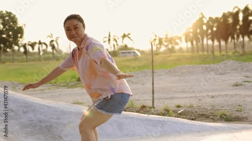 Attractive Asian woman with safety skateboarding knee pad skating at skateboard park .Female enjoy summer outdoor active lifestyle play extreme sport surf skate at public park.