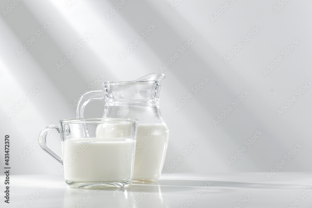 Natural milk in a glass vessel on a white background and a table in the morning sun Natural milk in a glass vessel on a white background and a table in the morning sun