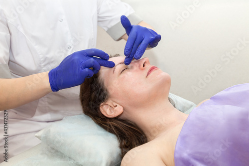 Cosmetologist hands in blue gloves touch face of caucasian woman patient making massage procedure in beauty salon.