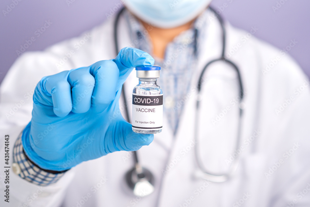 Doctor with a stethoscope on the shoulder wearing a face mask and holding a COVID-19 vaccine bottle. Vaccine for immunization, and treatment from coronavirus infection. Medical concept Doctor with a stethoscope on the shoulder wearing a face mask and holding a COVID-19 vaccine bottle. Vaccine for immunization, and treatment from coronavirus infection. Medical concept