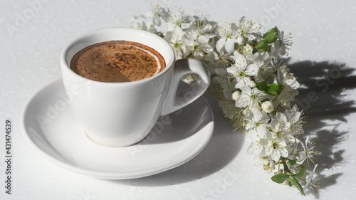 Obraz na płótnie White cup of coffee and spring blooming branch with white flowers on the white background in morning sunlight. Spring mood. Banner. w salonie