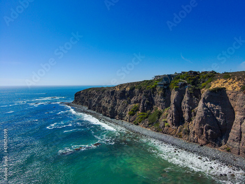 a stunning aerial shot of the coastline with vast blue and green ocean water, lush green hillsides with homes and waves crashing into the beach at Baby Beach in Dana Point California