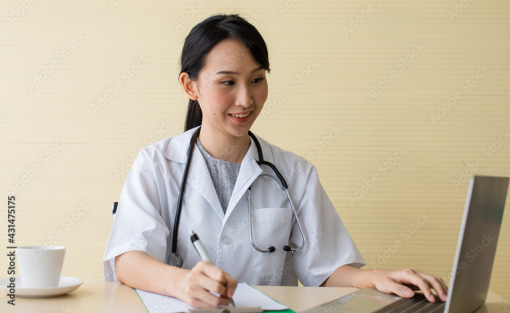 Woman doctor in uniform with stethoscope on neck sitting and writing on sheet board also use laptop to check patient list. As consultation young lady has successful job from many positive review. Woman doctor in uniform with stethoscope on neck sitting and writing on sheet board also use laptop to check patient list. As consultation young lady has successful job from many positive review.