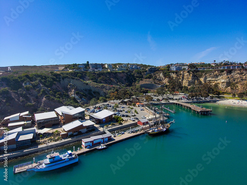 gorgeous aerial view of the boats and yachts in the Dana Point Harbor with vast blue and green ocean water, buildings along the harbor and majestic mountains and cliffs with blue sky in Dana Point CA