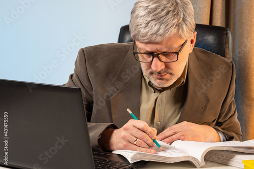 The auditor checks the documents. The businessman studies the payment schedule. A man is working on a project estimate. A man sits in front of a laptop and makes notes in the papers.