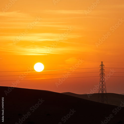 Dramatic sunrise over the Arabian Desert with power line and power pole near Abu Dhabi, UAE