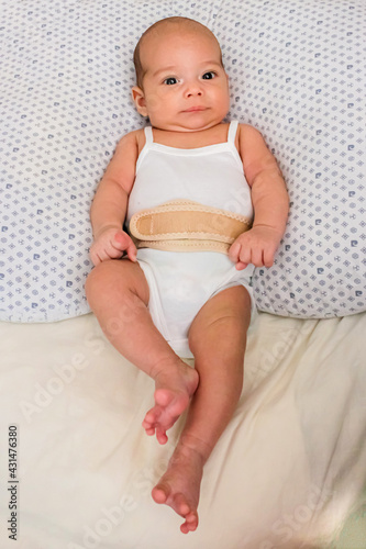 Baby in an umbilical hernia bandage. Sweet infant on the bed