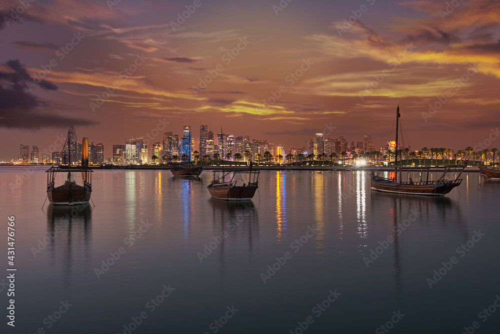 Doha Qatar skyline at dusk showing skyscrapers  lights reflected in the Arabic gulf and dhows in foreground with clouds  in the sky in background
