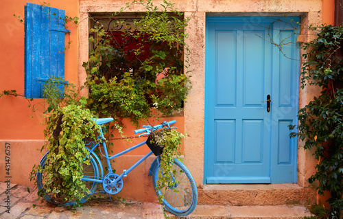 Rovinj, Istria, Croatia. Old blue bicycle at street near door of entrance in house among green bushes and flowerpots with flowers. Picturesque cosy lane. Window shutters on windows.