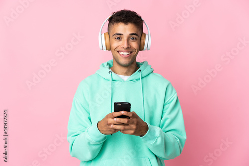 Young brazilian man isolated on pink background listening music with a mobile and looking front © luismolinero