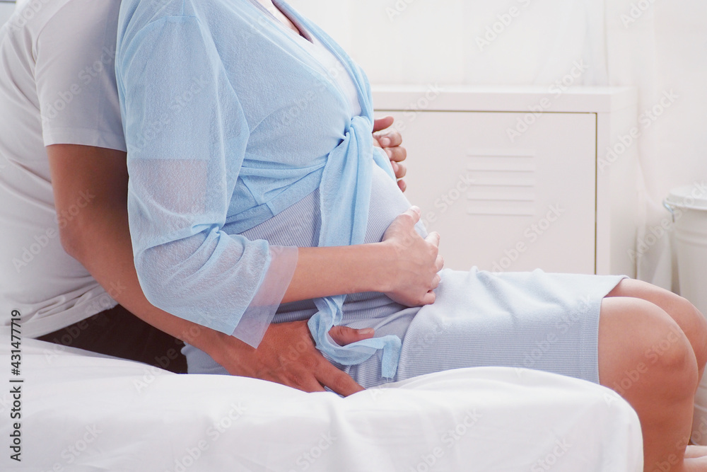 Warm moment of Asian man hugging and touching his pregnant wife on her tummy in their bedroom at home and expecting a cute baby soon Happy family lifestyle love husband and wife concept