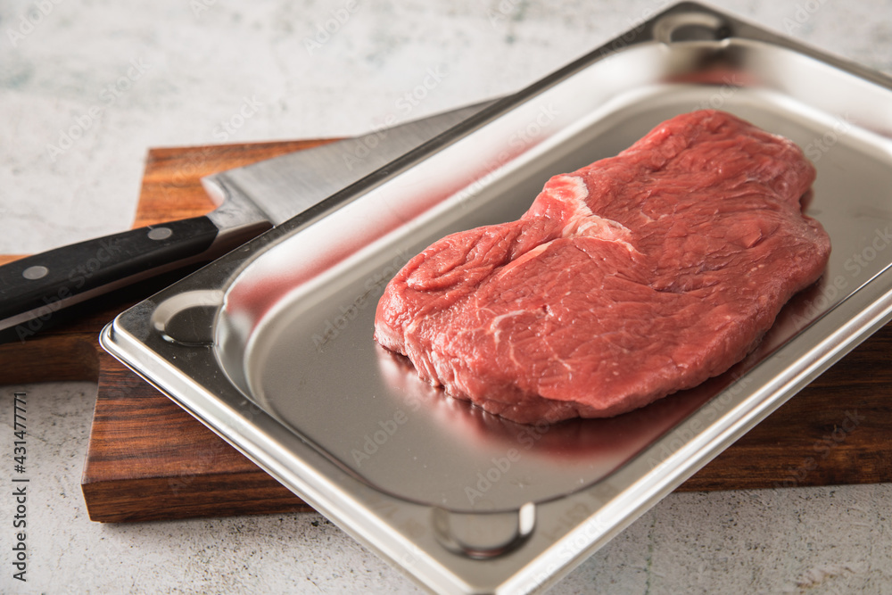 Rinder Steak roh auf Edelstahl Schale mit Küchenmesser, Holzbrett und Marmor Hintergrund hell