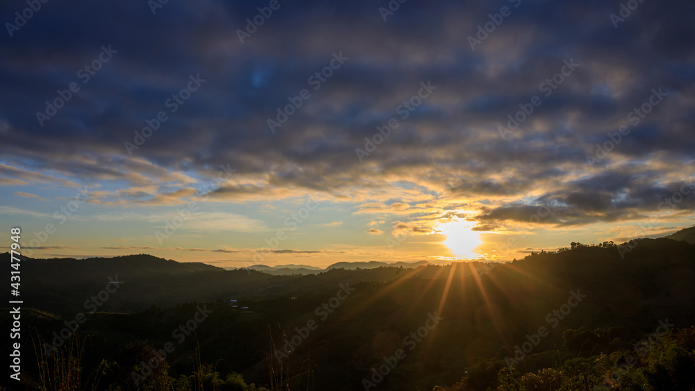 Sunset or evening time over clouds with mountain hill forest and sunlight sunrays or sunbeams on background.