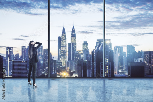 Businesswoman standing thinking in an empty big office room with big windows and night city view. Real estate and future success concept
