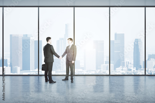 Two businessmen shaking hands in an empty big office room with big windows and city view, reaching an agreement. Communication and cooperation concept