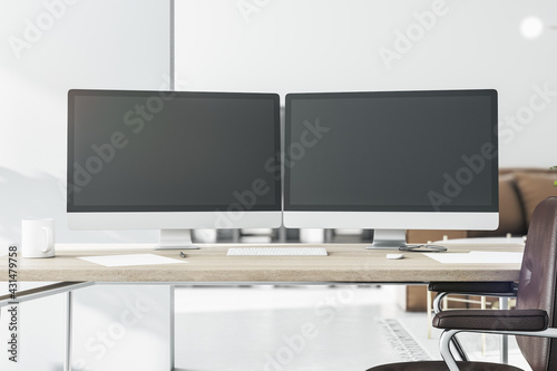 Stylish workspace with two black computer monitors with copyspace for your logo on wooden table in light sunny room. 3D rendering, mockup