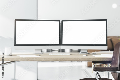 Blank white computer monitors on light wooden table with keyboard and brown leather chair near. 3D rendering, mock up