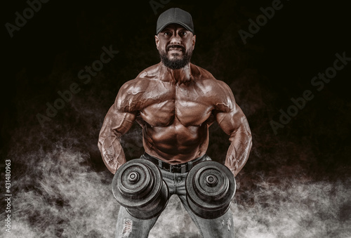 Muscular athlete lifts dumbbells. Shoulder pumping. Fitness and bodybuilding concept. photo