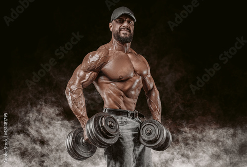 Muscular athlete posing in the studio with dumbbells. Fitness and classic bodybuilding concept.