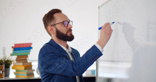 Young male teacher writing on board and explaining lesson to pupils