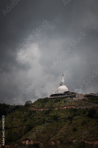 Mahamevnawa Buddhist Monastery temple in the mountain top low angle scenic landscape view. dark rainy clouds and cold atmosphere in Bandarawela, stupa glowing brightly in the distant hill.