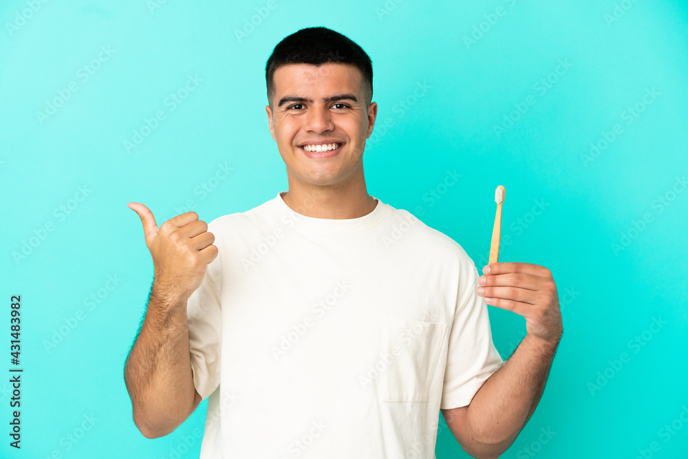 Young handsome man brushing teeth over isolated blue background pointing to the side to present a product Young handsome man brushing teeth over isolated blue background pointing to the side to present a product