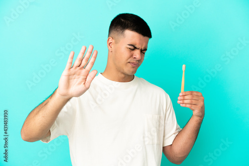 Young handsome man brushing teeth over isolated blue background making stop gesture and disappointed
