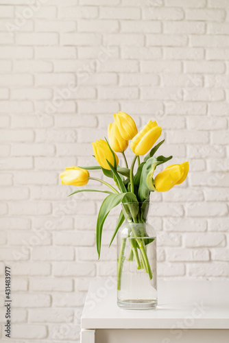 yellow tulips in a glass vase on a white brick wall background