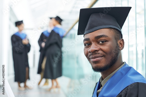 Close up portrait of young African-American man wearing graduation cap smiling at camera happily, copy space