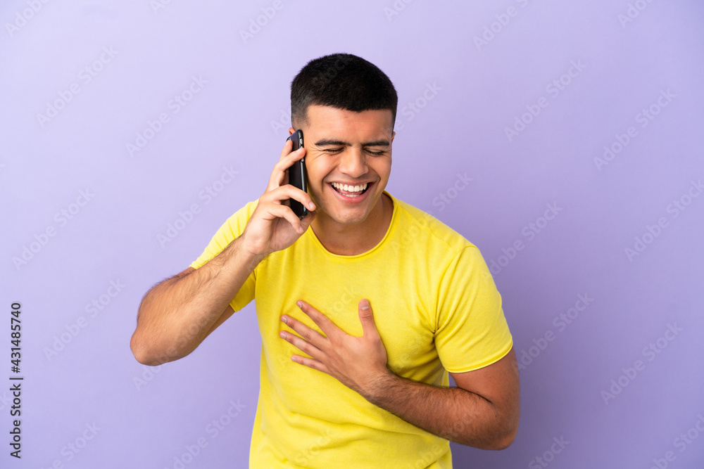 Young handsome man using mobile phone over isolated purple background smiling a lot Young handsome man using mobile phone over isolated purple background smiling a lot