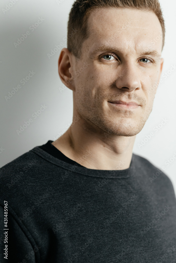 Fototapeta premium Close-up portrait of a young red-haired guy who is looking at the camera against the background of a gray wall. Place for your text.