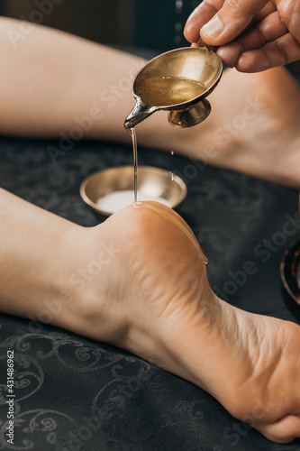 Close-up of hand pouring oil on leg. Oil applicator for relaxing massage. Gold body treatment and diamond powder exfoliating scrub.