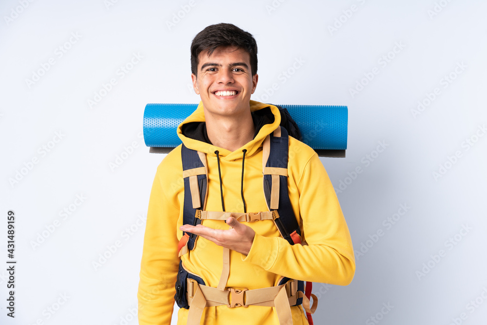 Young mountaineer man with a big backpack over isolated blue background extending hands to the side for inviting to come Young mountaineer man with a big backpack over isolated blue background extending hands to the side for inviting to come