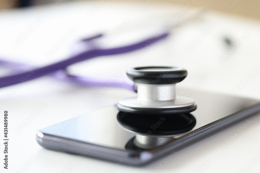 Medical instrument stethoscope lying on screen of mobile phone closeup Medical instrument stethoscope lying on screen of mobile phone closeup