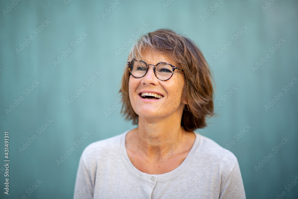 Fototapeta premium Close up happy woman with glasses laughing by green wall