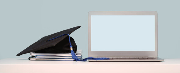 Graduation Cap on notebooks near laptop. Masters or Bachelors Degree thesis writing. Knowledge online courses qualifications and higher education with copy space. Lockdown. Mock up screen