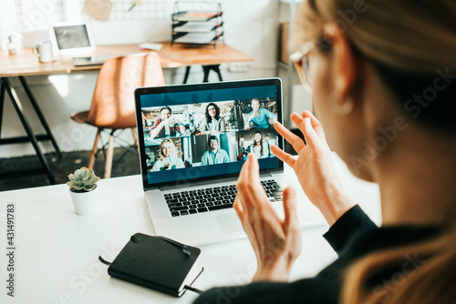 Woman has video call with her remote teammates using laptop.  White loft workspace