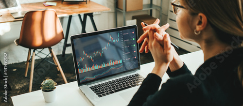 Woman working alone with stock market using laptop, analyzing trading data photo