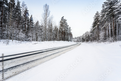 Snowfall on a winter day, snow-covered country road. View from the side of the road. Coniferous forest. Russia, Europe. Beautiful nature.