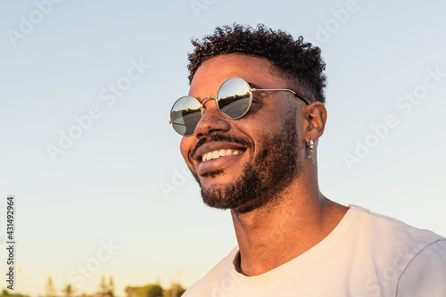 Face portrait of a handsome black and young american man wearing sunglasses and smiling during sunset at the beach
