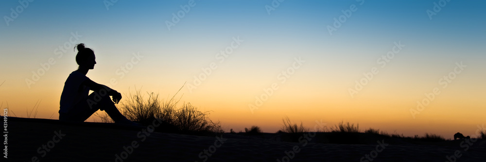 Silhouette of a woman sitting in the sunset, panoramic background
