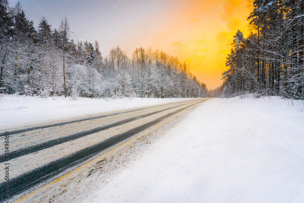 Sunrise on a clear winter morning, road passing through the forest in the snow. View from the side of the road. Coniferous forest. Russia, Europe. Beautiful nature.