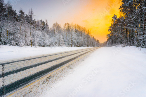Sunrise on a clear winter morning, road passing through the forest in the snow. View from the side of the road. Coniferous forest. Russia, Europe. Beautiful nature. © Georgii Shipin