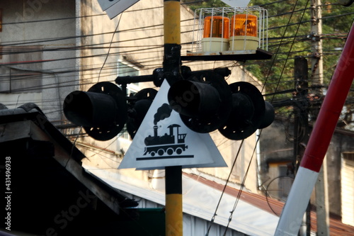 Railway crossing sign in triangle shape on pole, black picture train on white plate, Thailand.