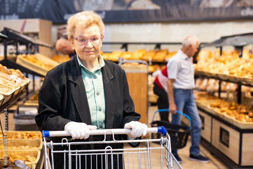 older european woman with glasses shopping in bread section of supermarket